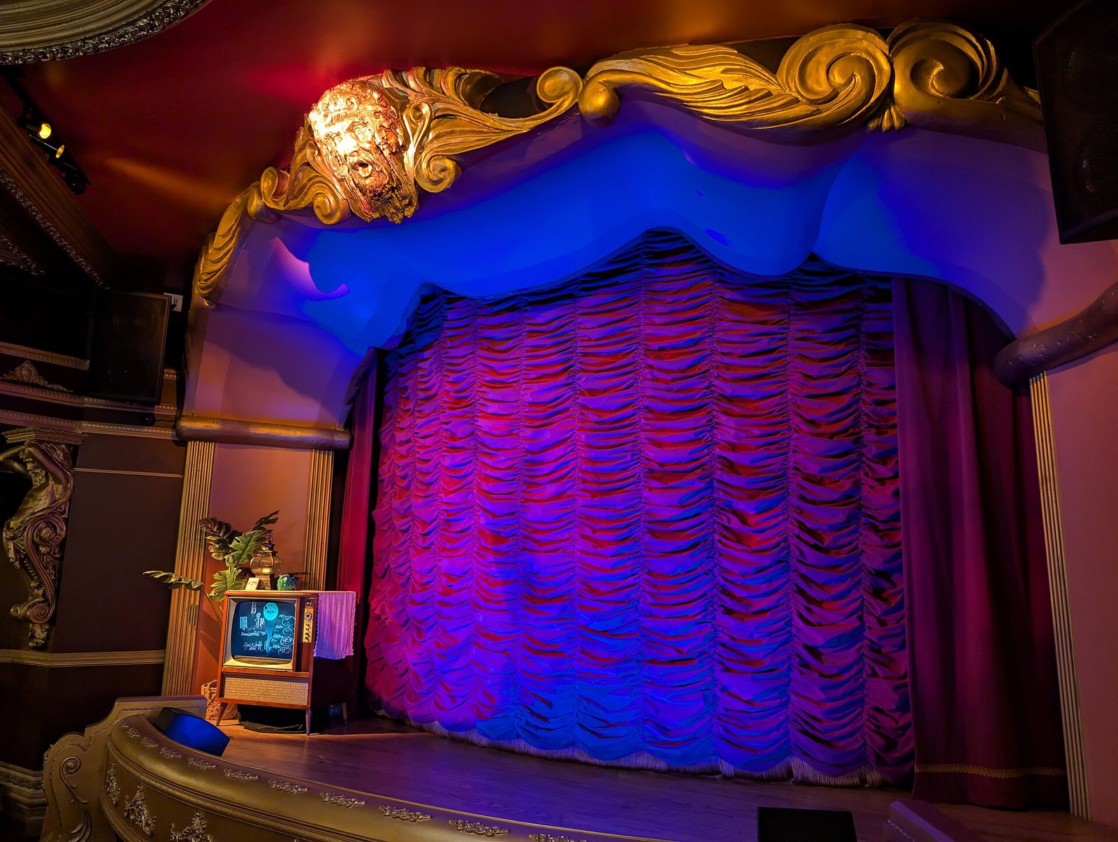The restored theater inside Casa Bonita in Lakewood, Colorado, with an ornate gilded proscenium arch and a blue and purple lit stage curtain