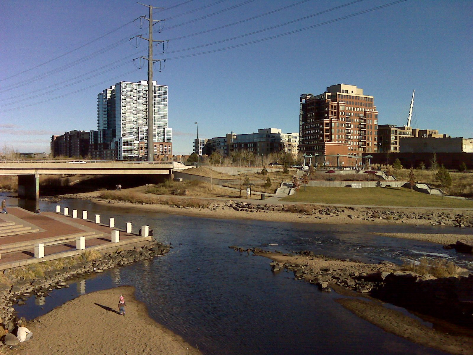 Cherry Creek meeting the South Platte River at Confluence Park in Denver, with stepped brick terraces down to the water, a sandbar in the river and apartment towers behind