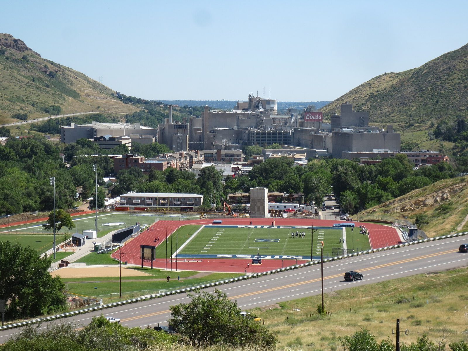 The Coors brewing complex filling a valley in Golden, Colorado, with the Colorado School of Mines football field in the foreground and hogback ridges on either side