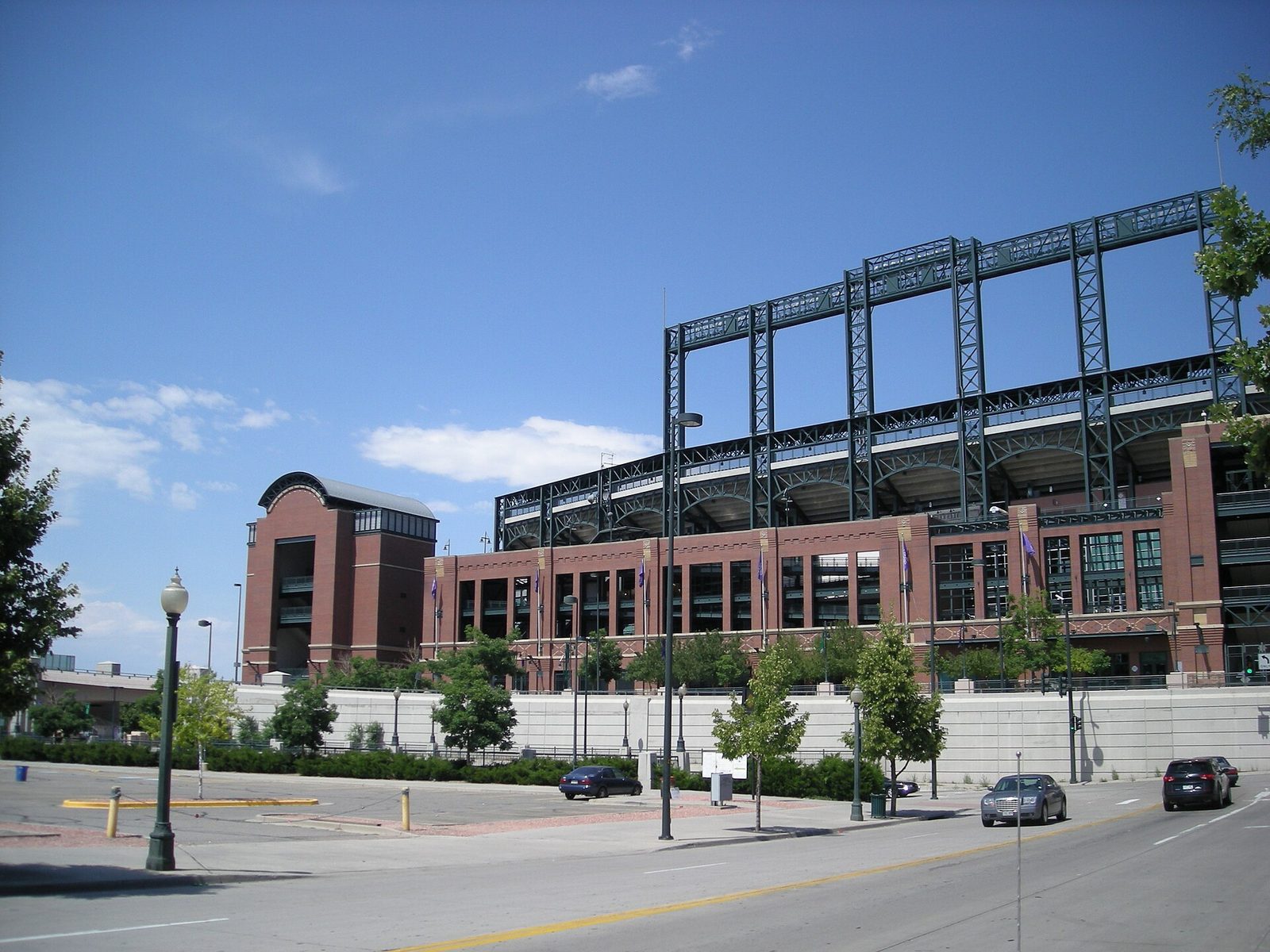The brick and green-steel exterior of Coors Field in Denver seen from a street corner, with light towers above the upper deck