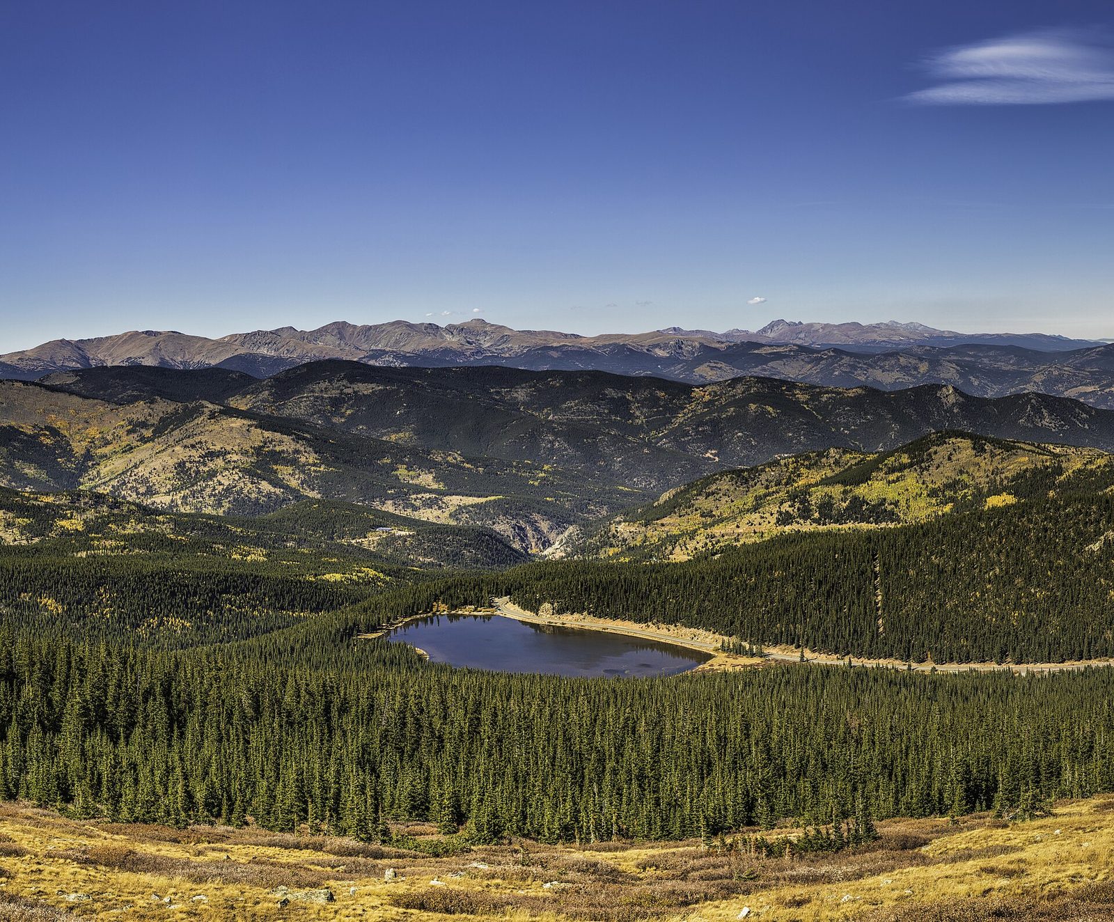 Echo Lake seen from high on the Mount Blue Sky road in early fall, ringed by dark conifer forest with aspens turning gold on the ridges and the Continental Divide on the horizon