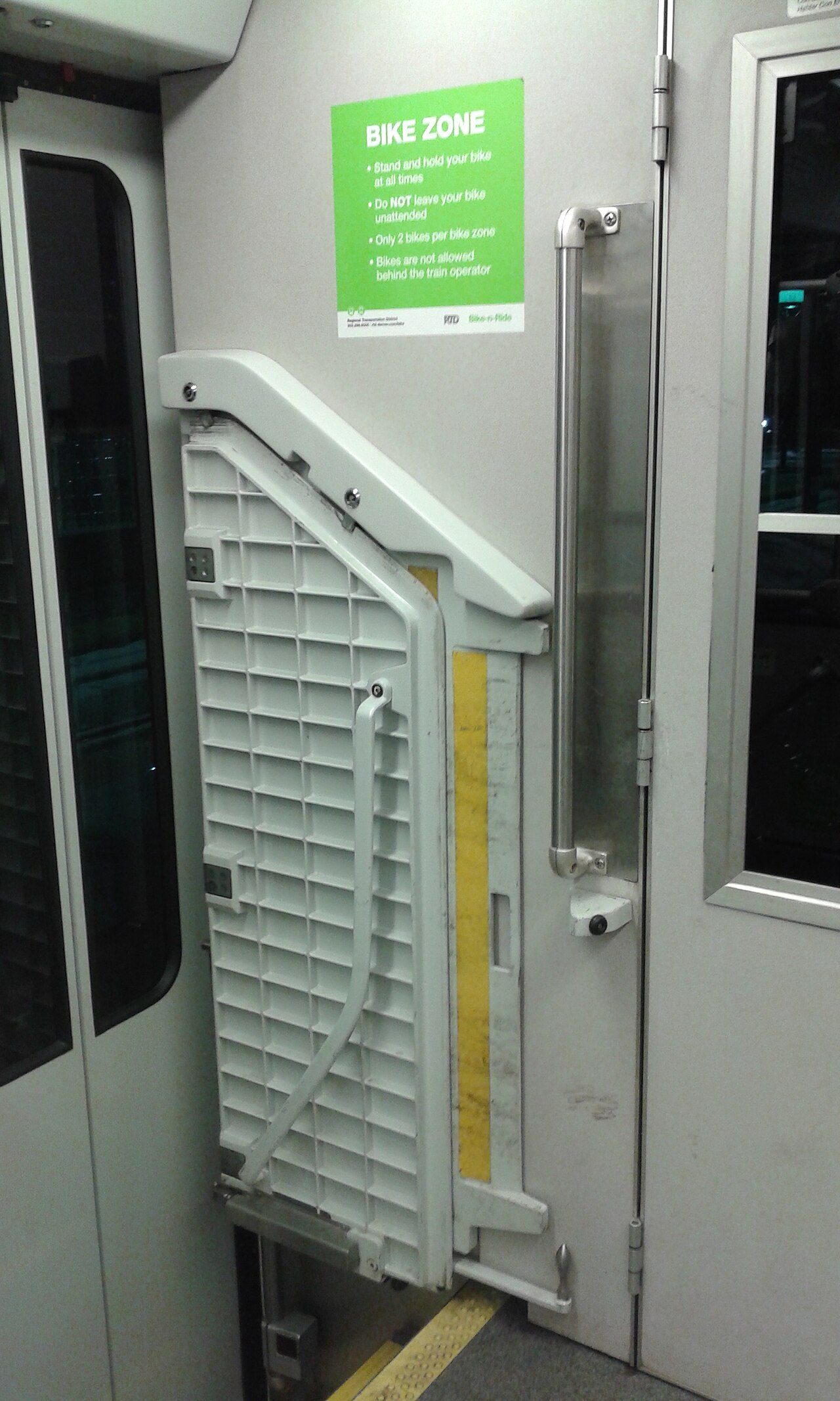 A green Bike Zone sign inside an RTD light rail car listing rules to stand and hold your bike, not leave it unattended, only two bikes per zone and no bikes behind the train operator