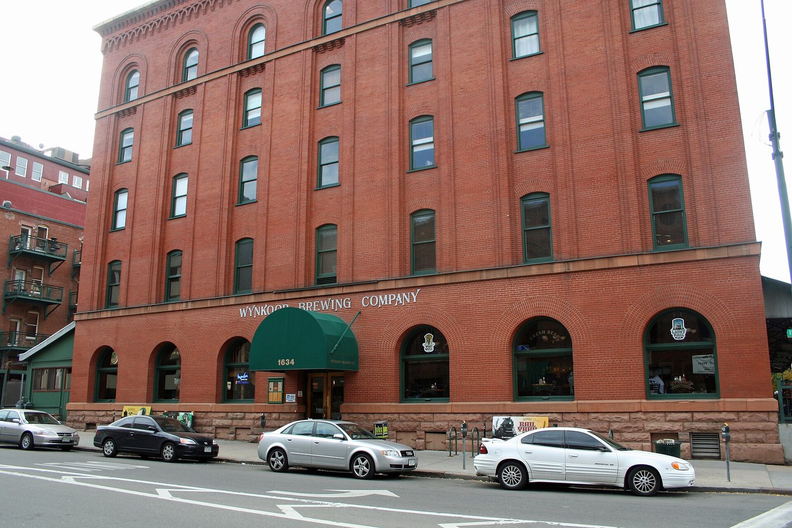 The red brick five-story Wynkoop Brewing Company building on a corner in LoDo Denver, with arched ground-floor windows, a green awning and the company name in lettering across the facade