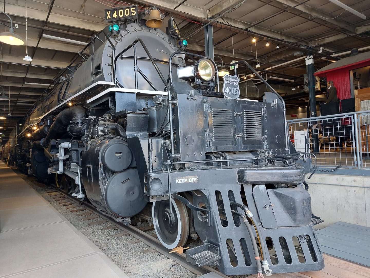 The front of Union Pacific Big Boy steam locomotive number 4005 inside the Forney Museum of Transportation in Denver, a massive black engine with a headlight and number plate, beside a visitor platform under a warehouse roof