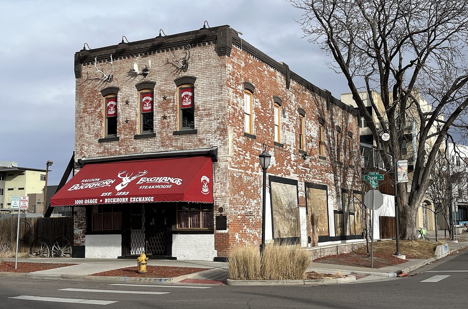 The Buckhorn Exchange in Denver, a two-story red brick building with antlers mounted along its roofline and a red awning reading Saloon, Buckhorn Exchange, Steakhouse, Est. 1893, at the corner of Osage Street